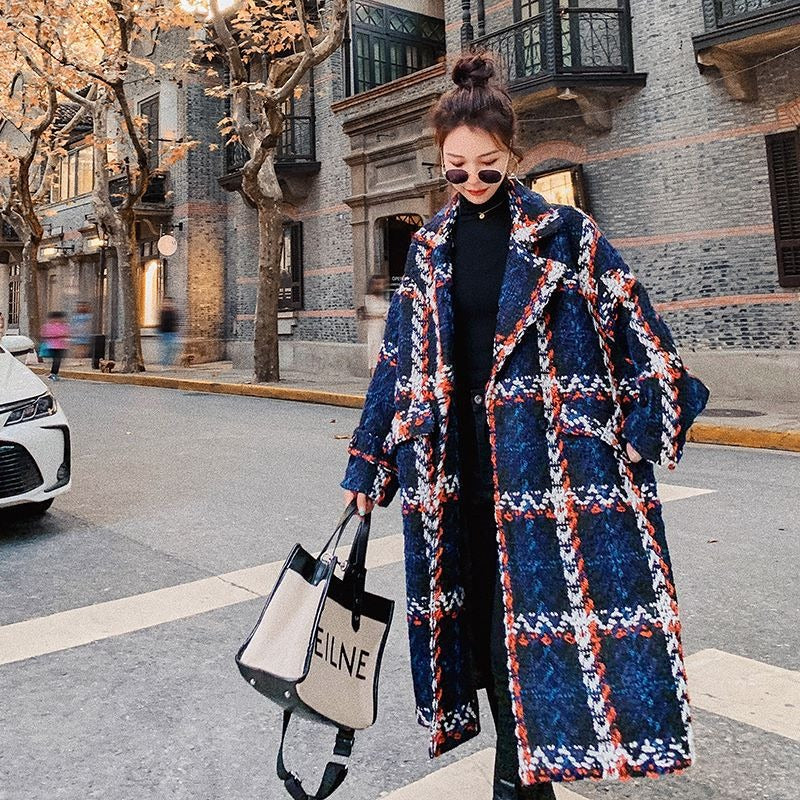 A woman wearing a mid-length blue, orange, and white plaid woolen coat on a street.