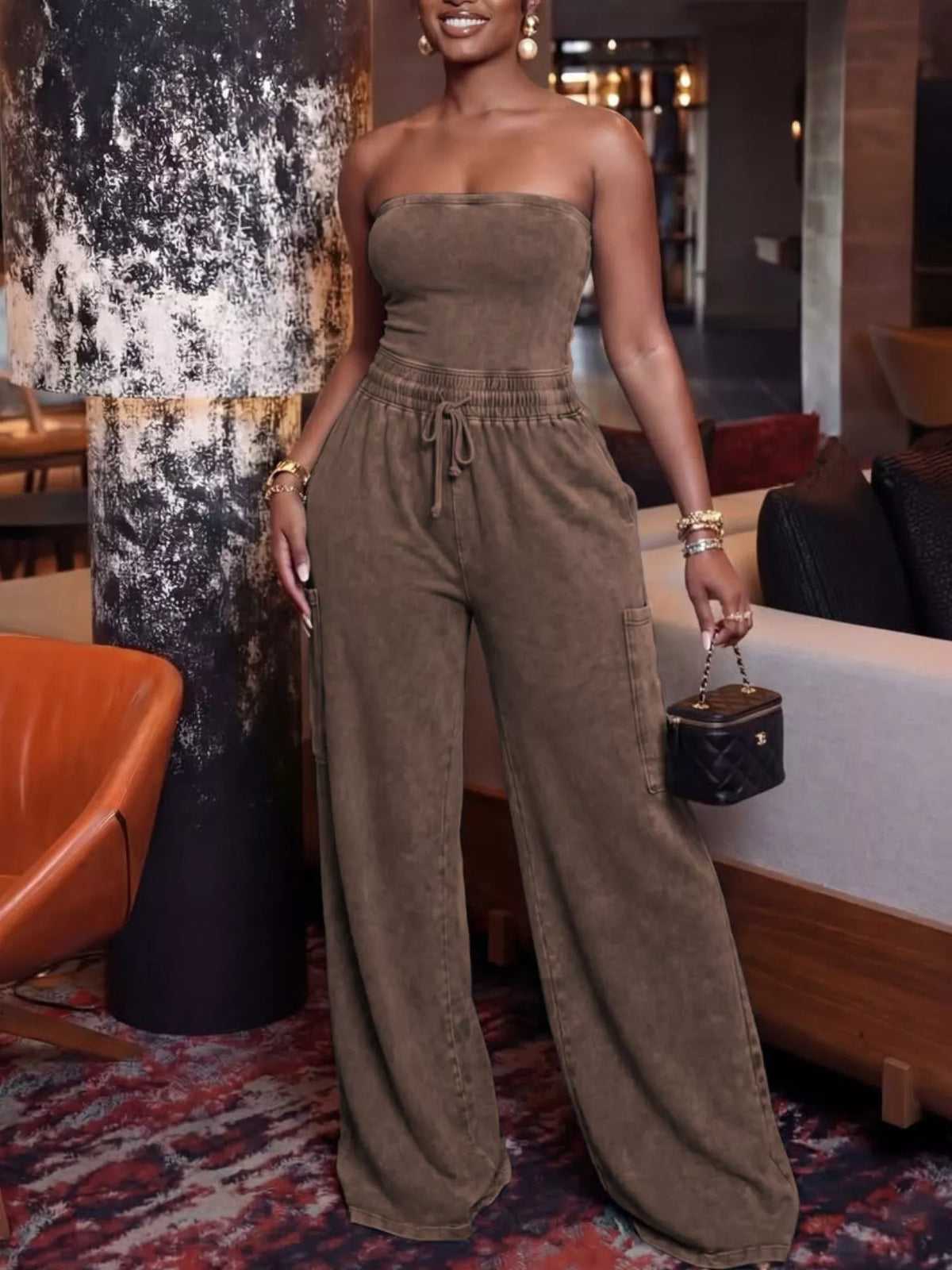 Strands strapless wide-leg jumpsuit from Trendsi with drawstring waist, flowing fabric, and relaxed fit, suitable for casual or evening wear.