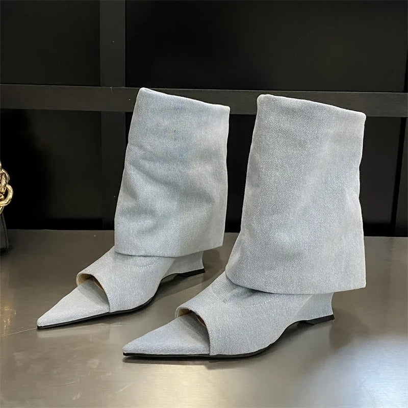 Light blue denim peep-toe wedge boots with a folded slouchy cuff and pointed toe, set on a dark surface.