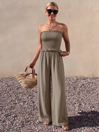 Smocked strapless wide-leg jumpsuit by Trendsi featuring a fitted bodice and flowing wide-leg pants, displayed on a hanger.