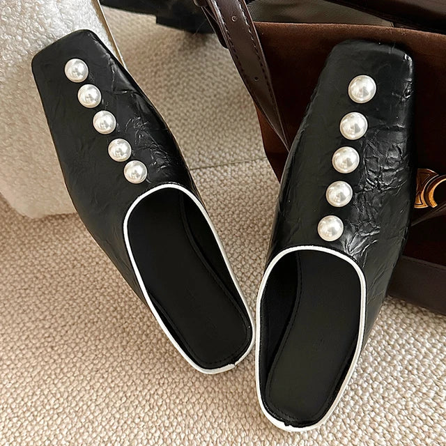 Black square-toe slide sandals in crinkled faux leather, featuring pearl embellishments and white piped trim.