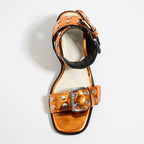 Metallic orange mid-heel sandal with silver rivets, buckled straps, and a square toe on a white background.