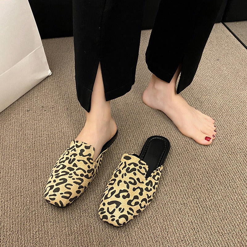 Beige and black leopard print pointed-toe mules with black insoles, worn with black split-hem trousers.