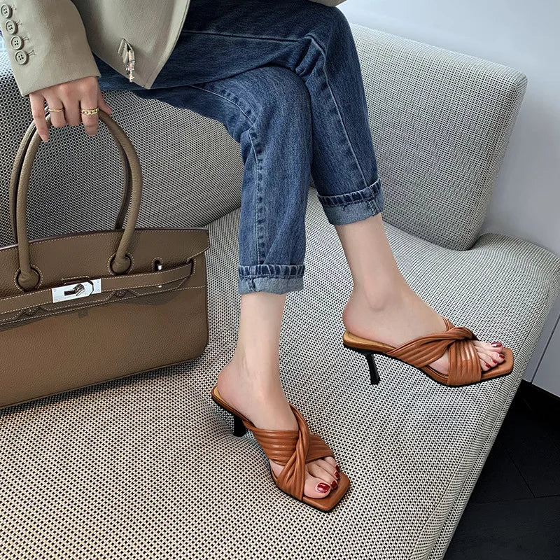 Tan square-toe stiletto mule heels with quilted crisscross straps, worn with cuffed jeans and a matching handbag.