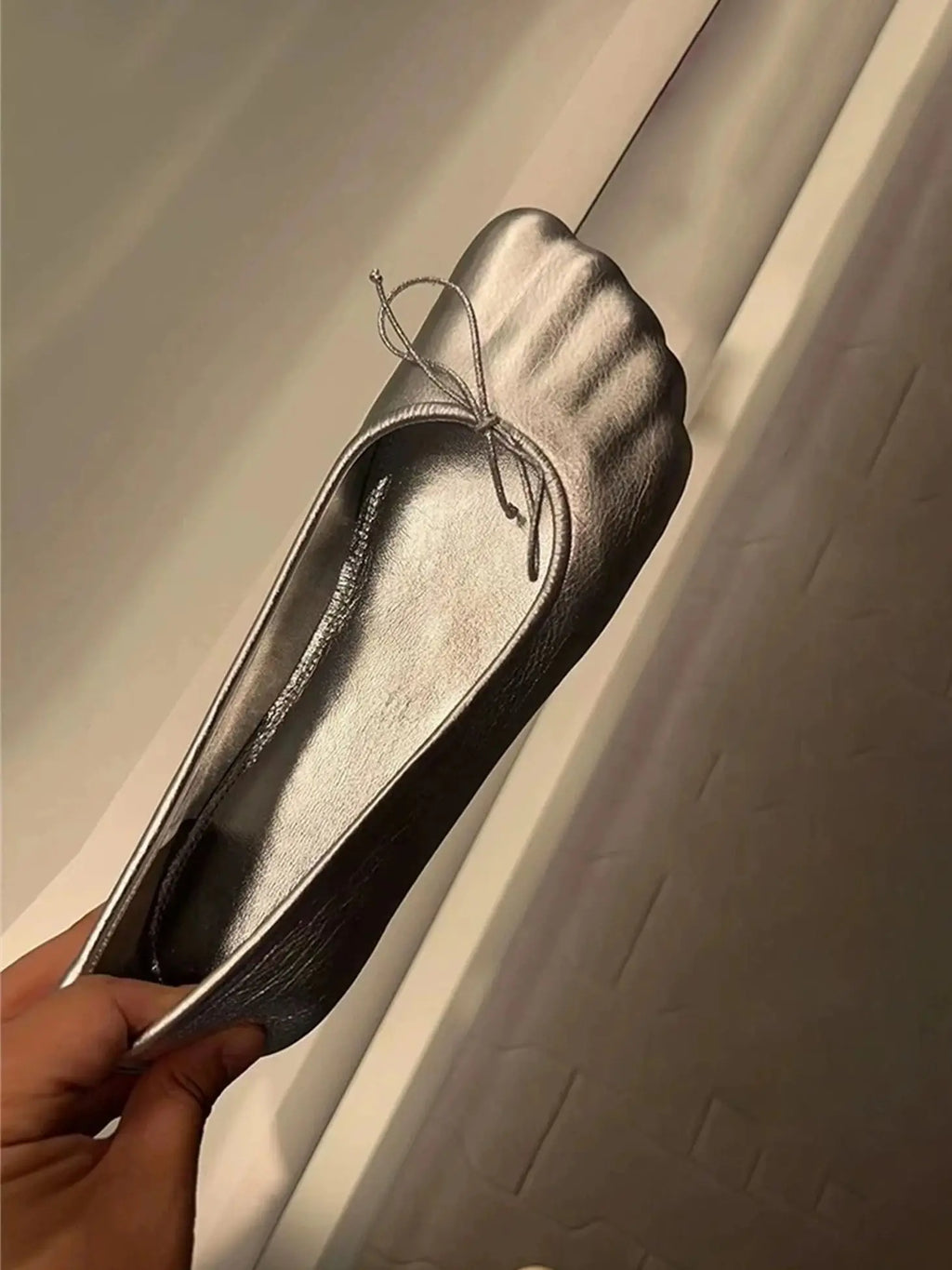 Metallic silver ballet flat with a soft, round toe, pleated front detail, and a delicate tie bow accent.