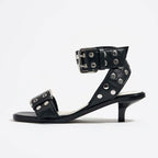 Black leather strappy mid-heel sandals with silver metal rivets and buckle closures.