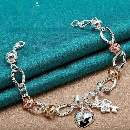 Silver Love Key Bracelet with heart-shaped charm and ethnic design on teal surface.