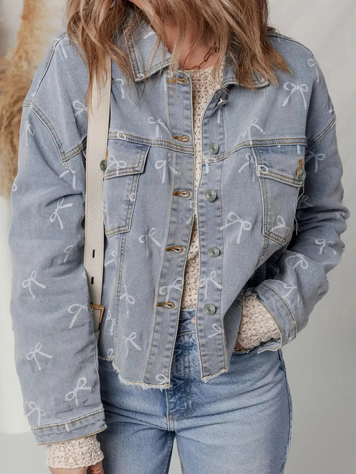 Women’s light wash denim jacket with bow knot print and raw hem, by Plush Fashion Hub.