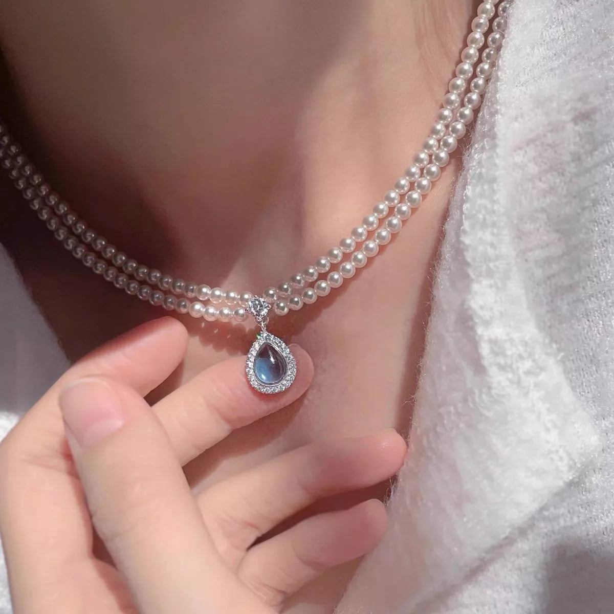 Double layered pearl necklace with teardrop pendant, featuring elegant white pearls and a delicate gold chain, by Plush Fashion Hub.