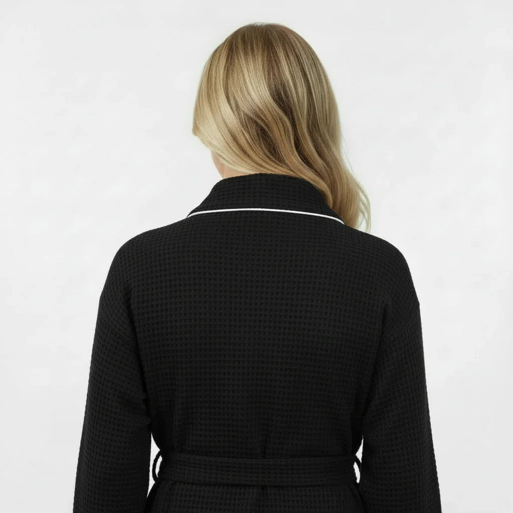 Back view of Lotus Linen women's knee-length black waffle robe with piping, showcasing its cozy fabric and tailored fit.