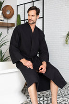 Men's Lotus Linen waffle spa bathrobe made of absorbent, lightweight cotton, shown hanging with a soft, textured fabric.