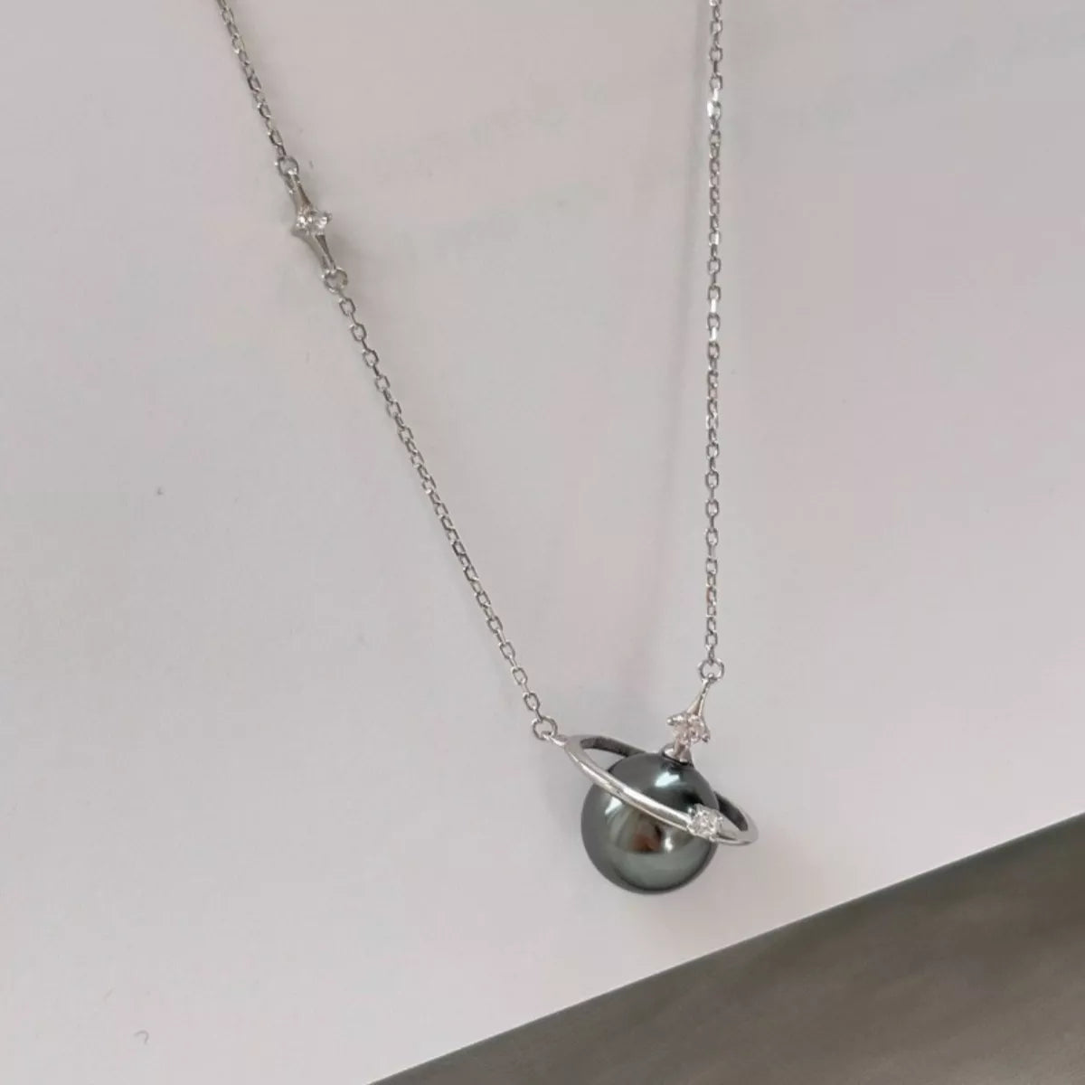 Plush Fashion Hub Planet Pearl Pendant Necklace featuring a shimmering pearl pendant on a delicate chain against a neutral background.