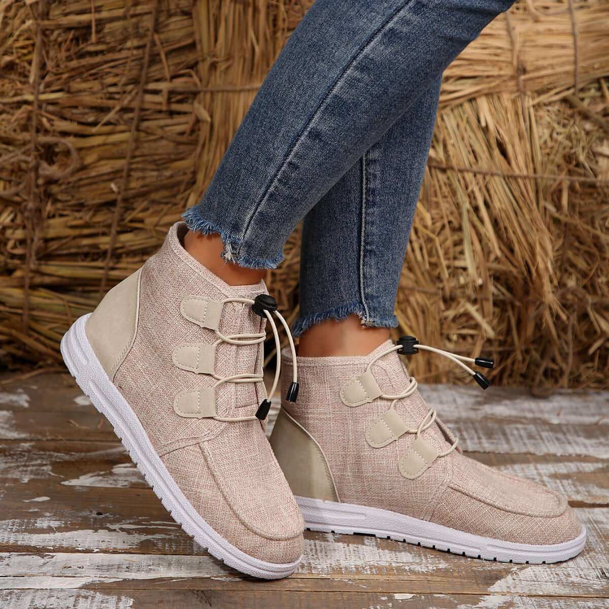 Round Toe Flat Sneakers in beige with lace-up design on wooden background.