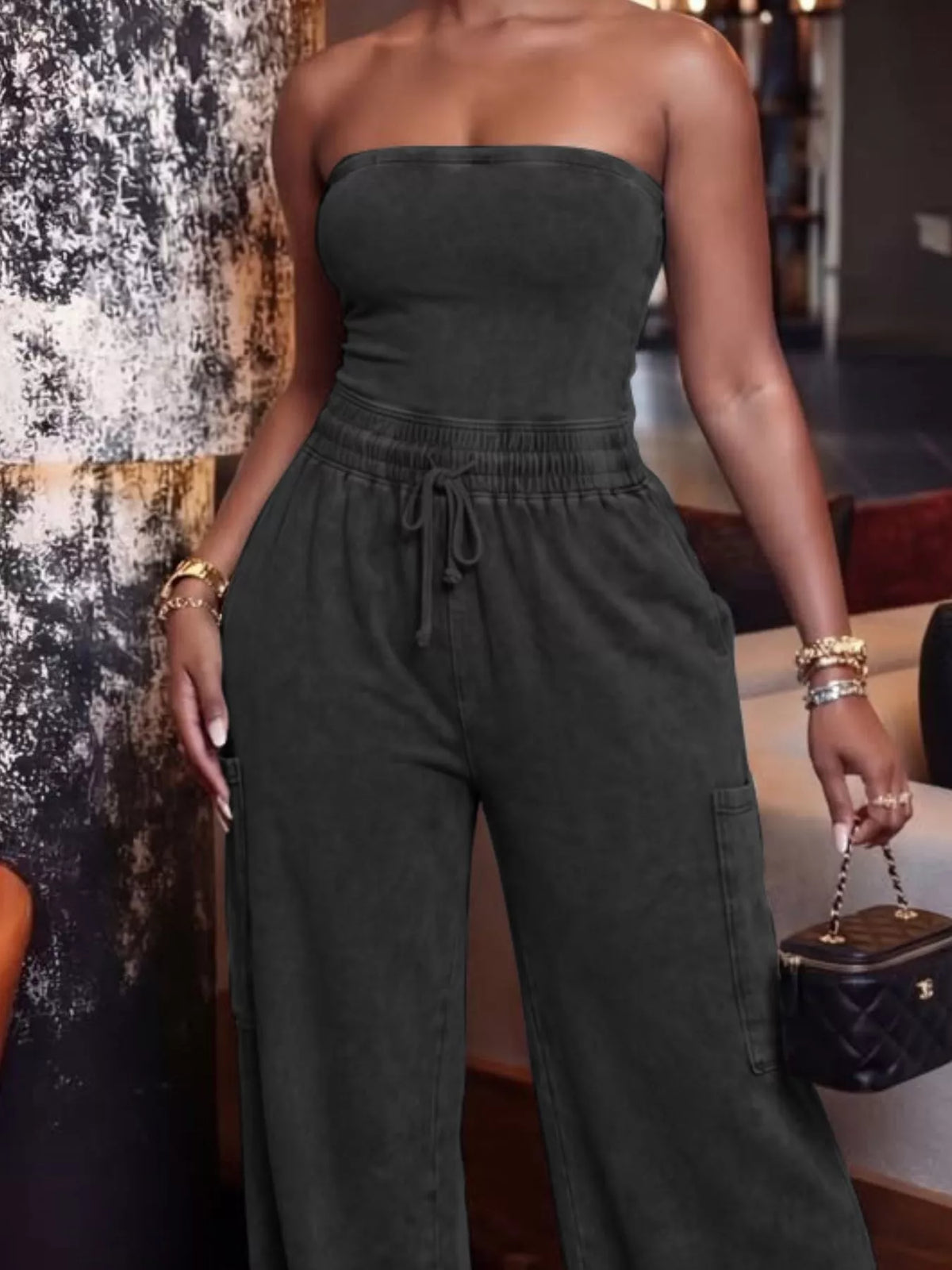 Black drawstring strapless wide-leg jumpsuit from Trendsi, featuring a fitted bodice and flowing wide-leg pants.