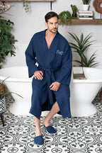 Lotus Linen men's waffle spa bathrobe, lightweight and absorbent, shown hanging on a hook in a cozy bathroom setting.